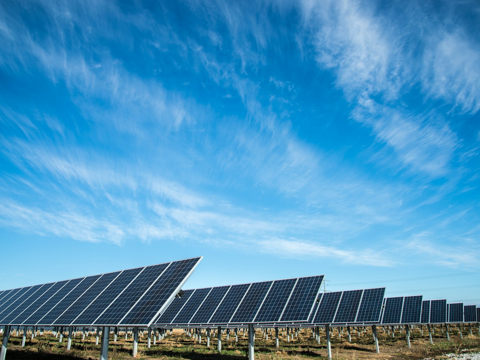 Filas de seguidores fotovoltaicos en una planta solar sobre suelo, bajo un cielo con cirros.